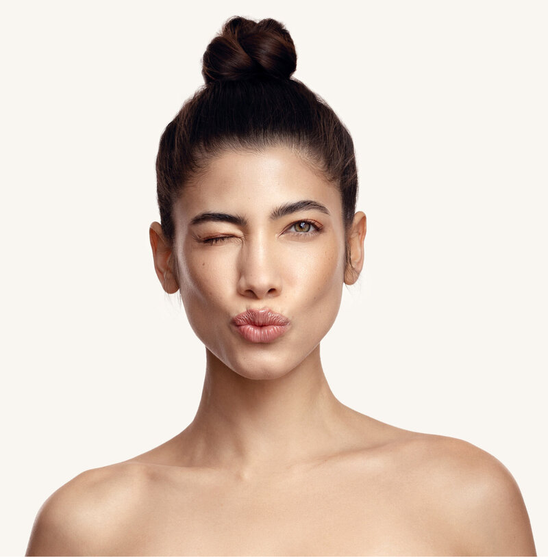 Apoorva in a playful YSL beauty portrait, making a fun facial expression with a natural, minimalistic background, captured by Ylva Erevall.