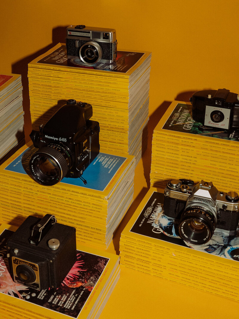 Stack of National Geographic magazines with film cameras placed on top