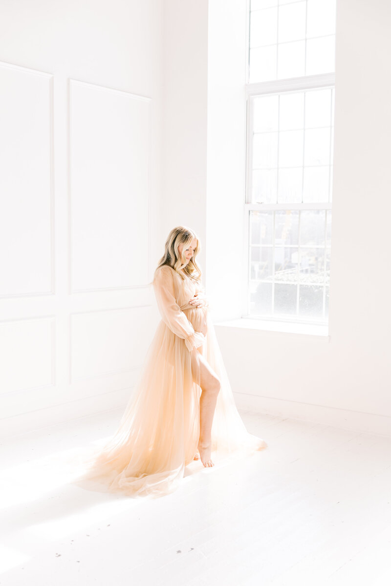 A mother to be pops a leg while smiling down at her bump in a studio window