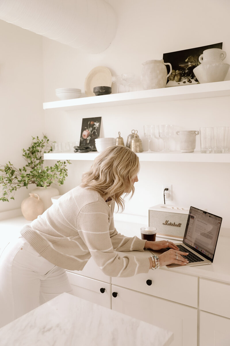 Molly Rubesh leaning against a counter in the kitchen on her computer