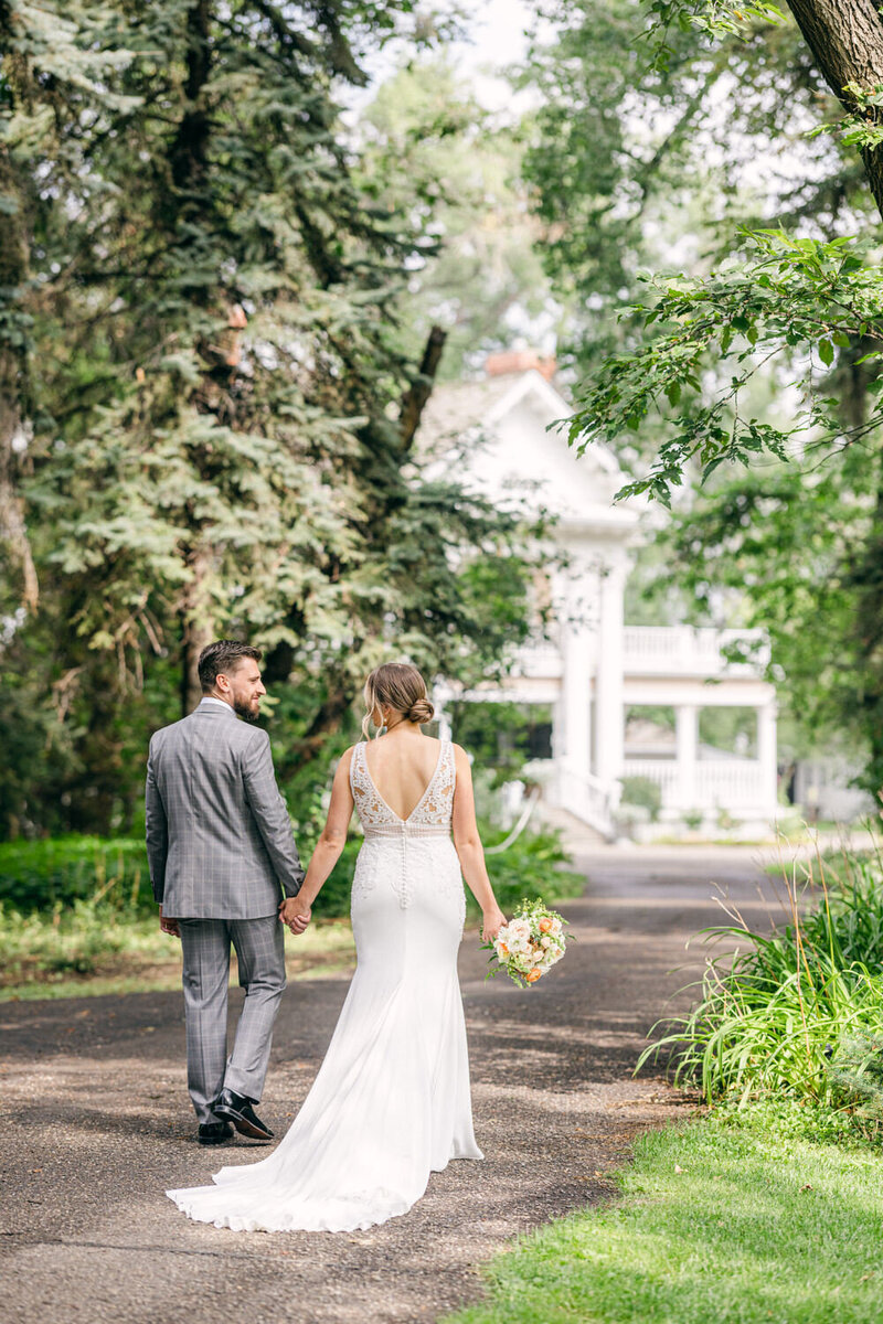 Capture the happiness of a bride and groom walking hand in hand, smiling as they approach a historic estate. A beautiful moment of love and joy on their special day.