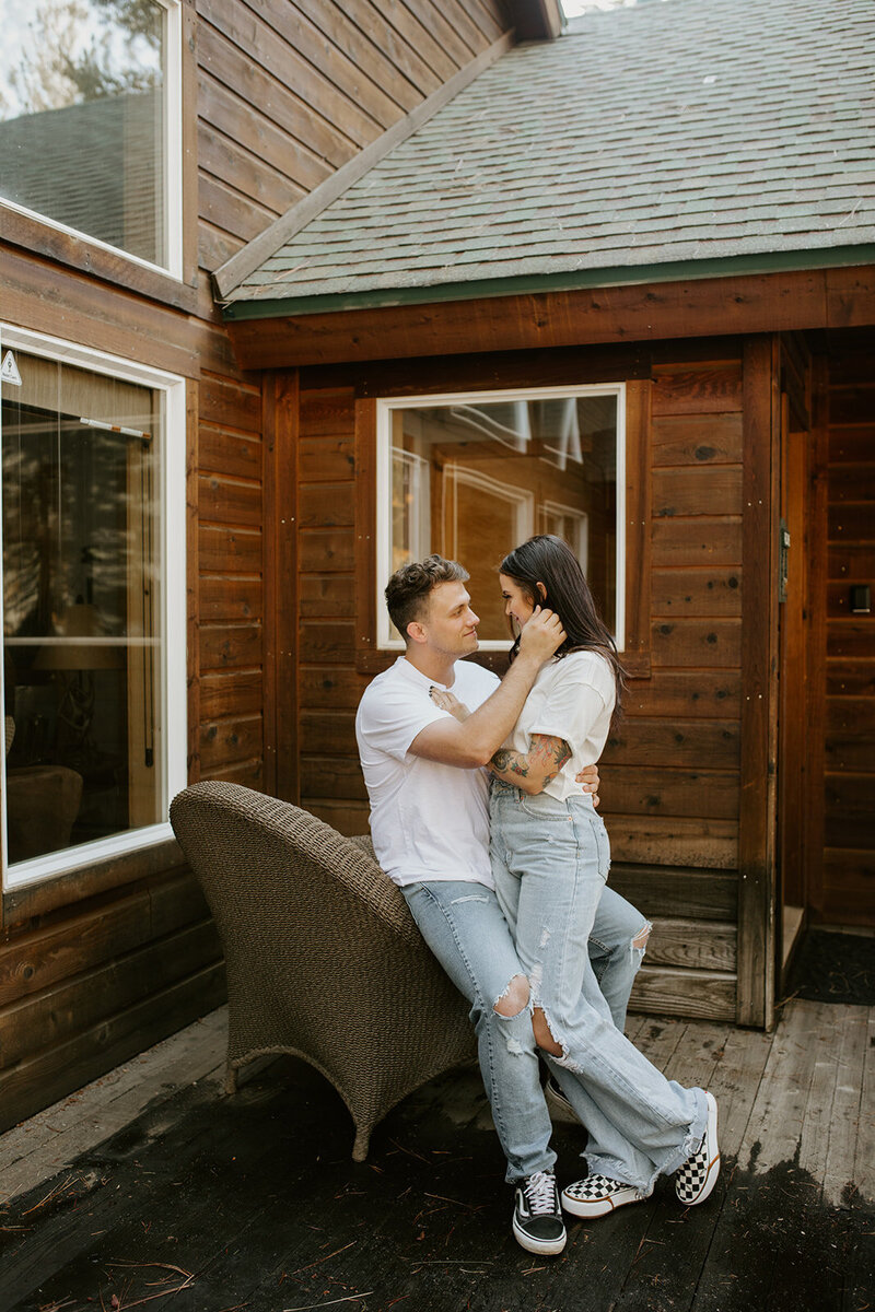 Couple leaning in and looking at each other while sitting in front of Oklahoma cabin