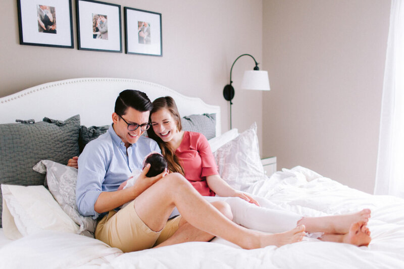 Mom and Dad Smiling at Newborn Baby on Bed