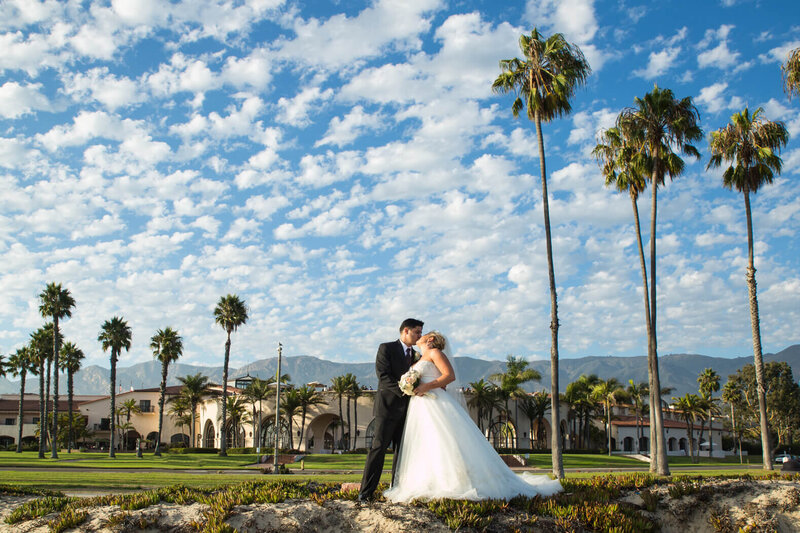 Bride and groom embracing for a kiss with palm trees and mountains behind them at the Fess Parker hotel in Santa Barbara, captured during their First Look wedding photo timeline.
