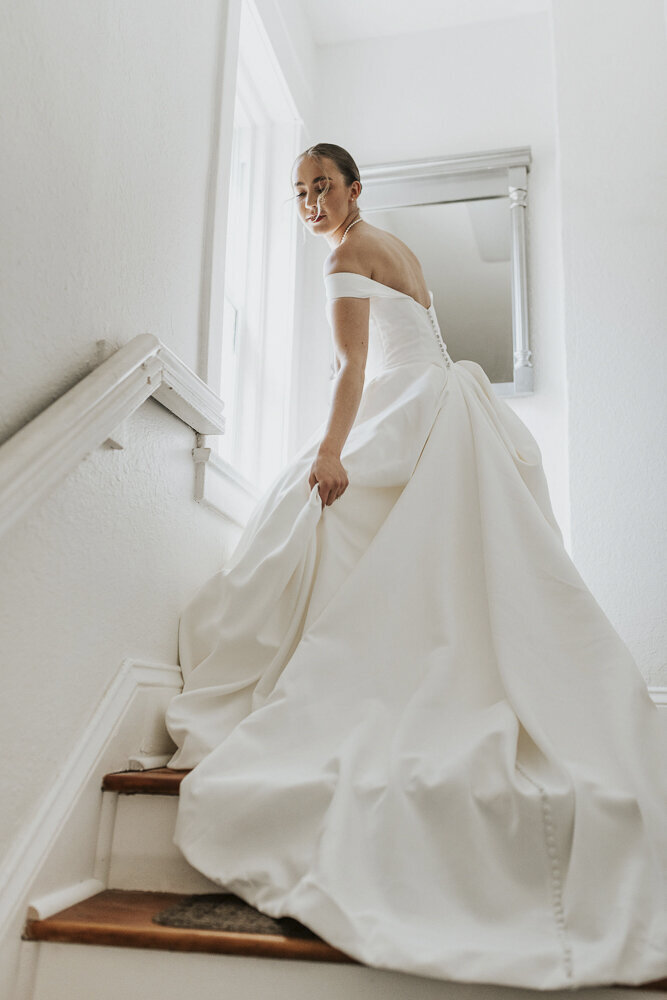 a bride holding her dress while standing at the top of stairs