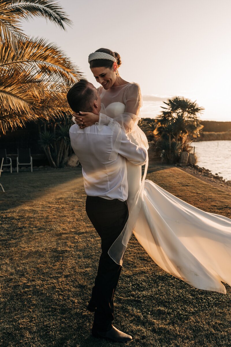 groom spins bride in hera couture and trish peng beside a lake at sunset in their christchurch wedding photos