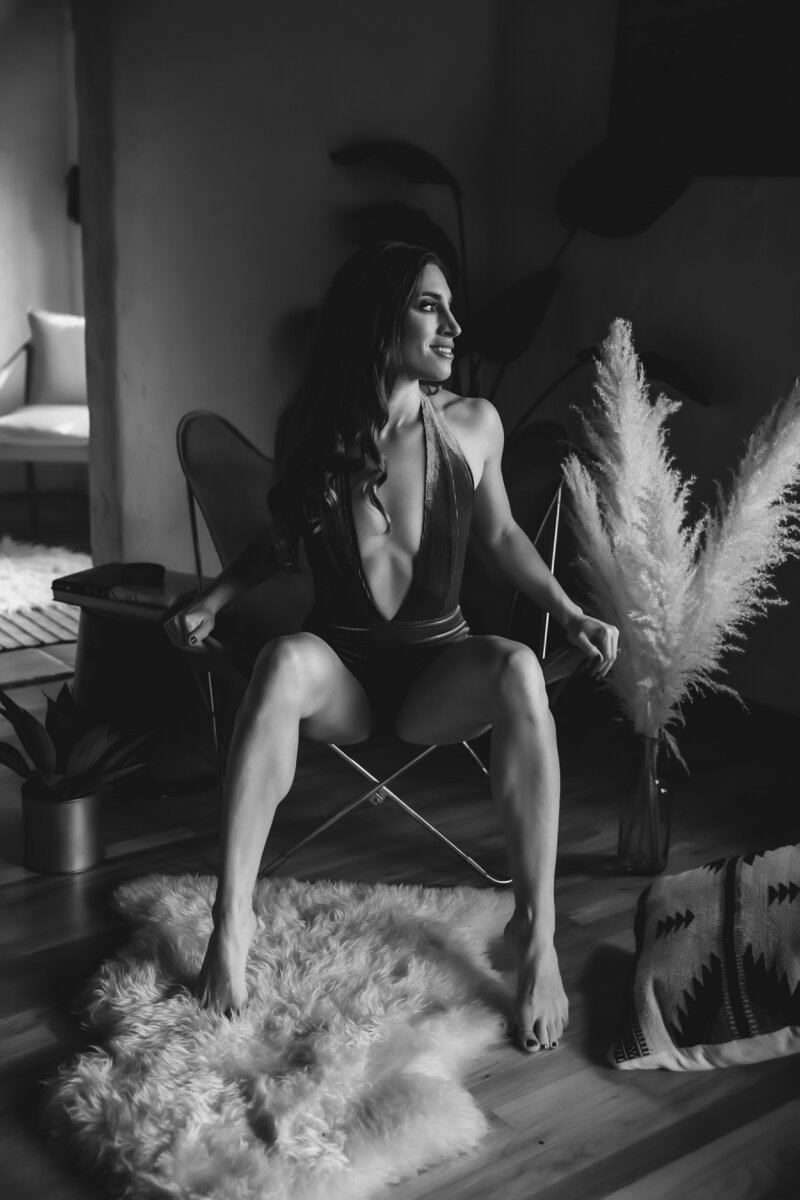 Black and white portrait of woman sitting in a chair looking out to her left smiling