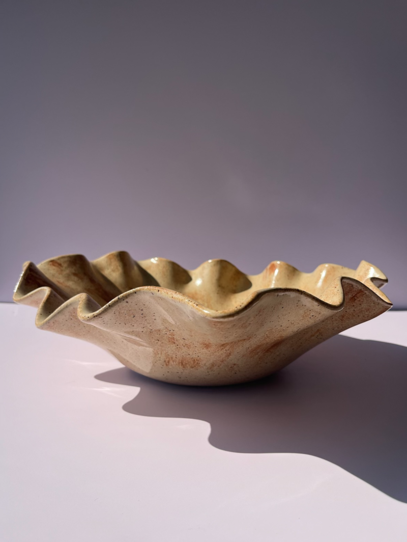 A beige and brown speckled ceramic wave serving bowl sits on a white table