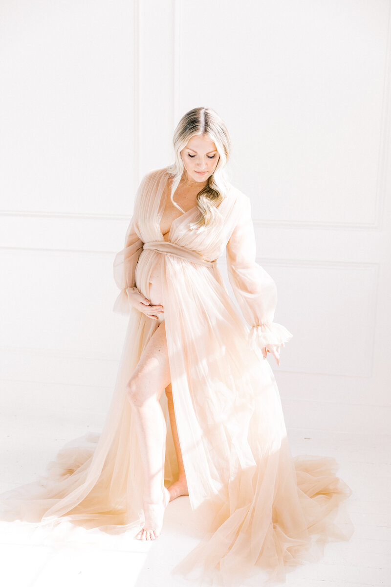 Pregnant woman in a flowing blush gown, captured in a soft, studio maternity session in Charlotte NC.