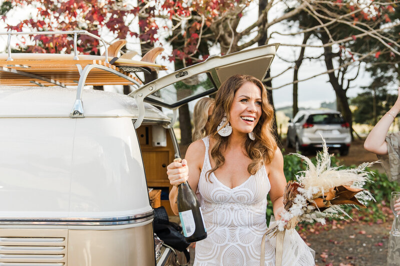 bride with bottle of bubbles in front of kombi van