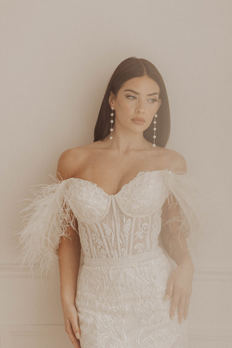 Contemplative bride in detailed gown, soft-lit portrait.