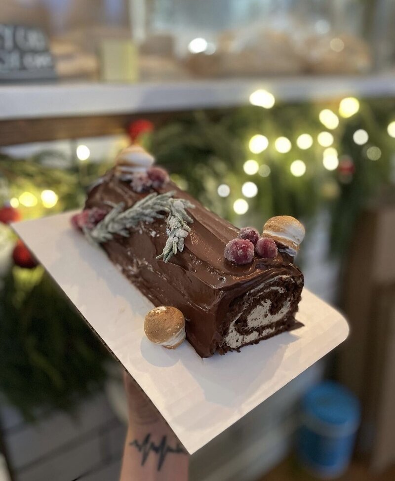 Gluten-free yule log or gluten-free buche de noel with sugared cranberries and meringue mushrooms, a gluten-free version of a traditional French Christmas cake available for preorder.