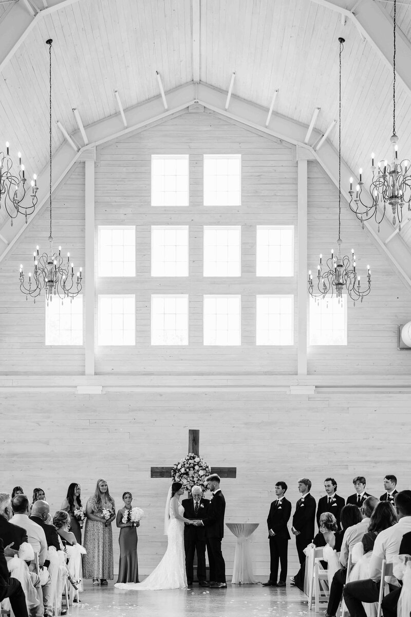 bride and groom holding hands at wedding alter in a big white church with bridal party on either side and wedding officiant behind them