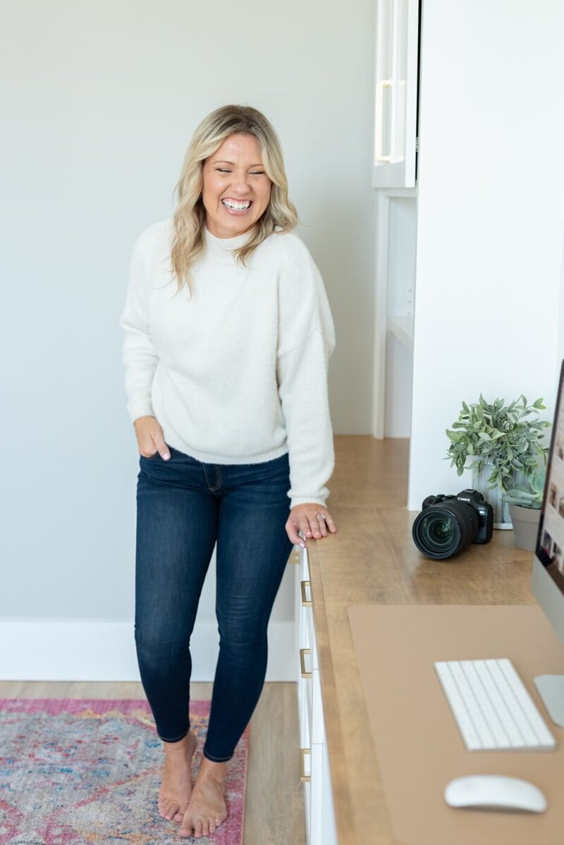 Tara Dunn, brand photographer, laughing beside her camera in her office