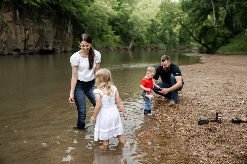 Parents with their two kids playing in the river and on the rocky beach with bluffs in the background taken in Bonne Terre, Missouri. 