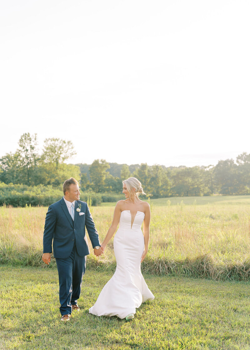 bride and groom holding hands while standing in a field
