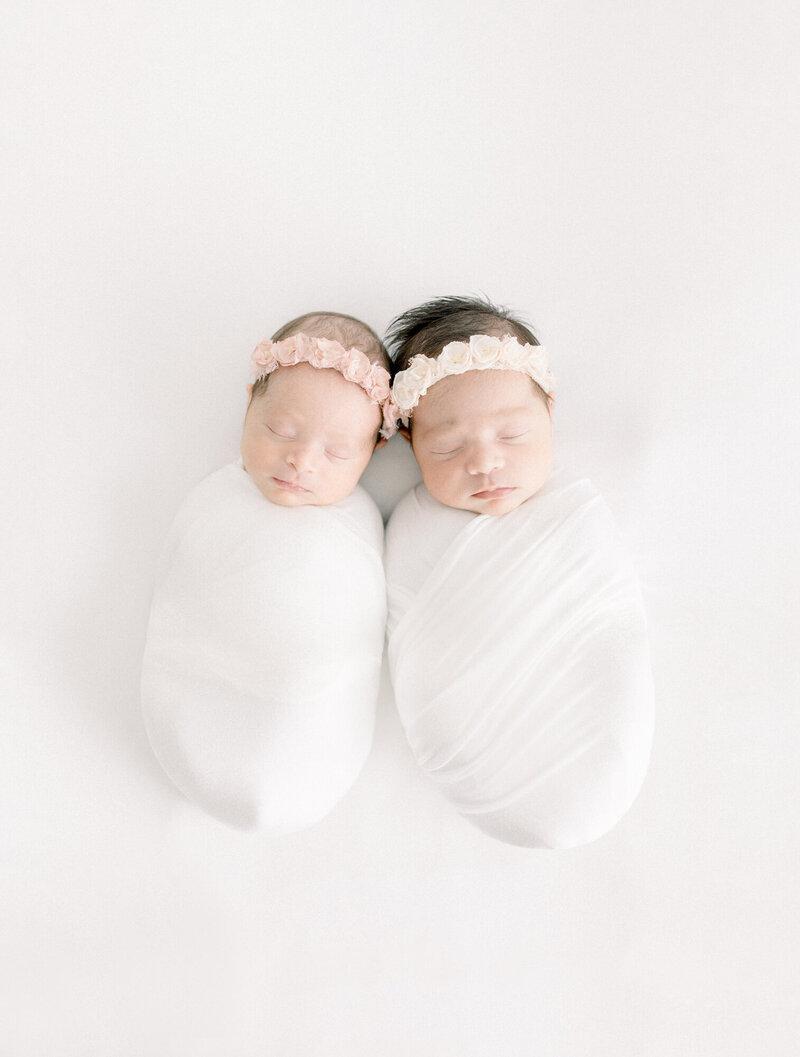 Twin baby newborn girls swaddled and snug together as they are posed laying down in a las vegas photography studio