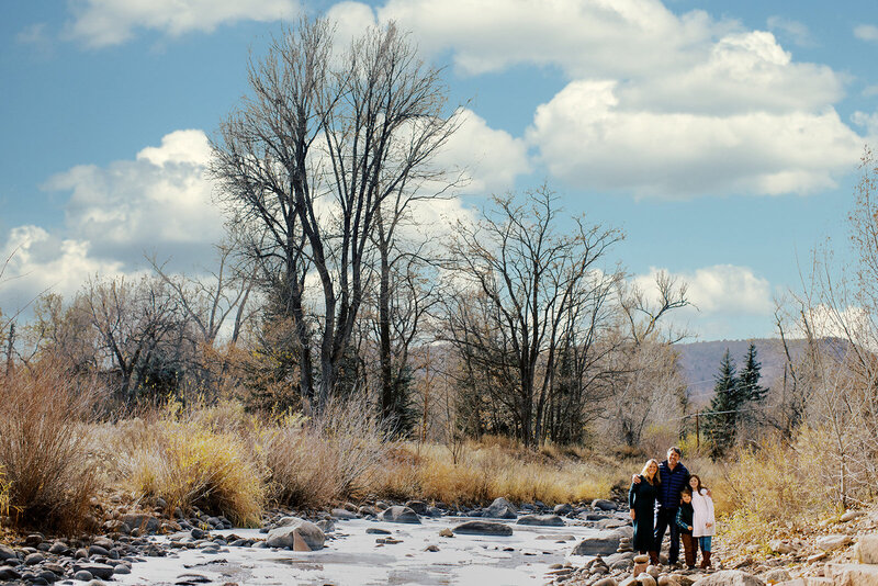 family of four stand by a river in lyons colorado on a winter day