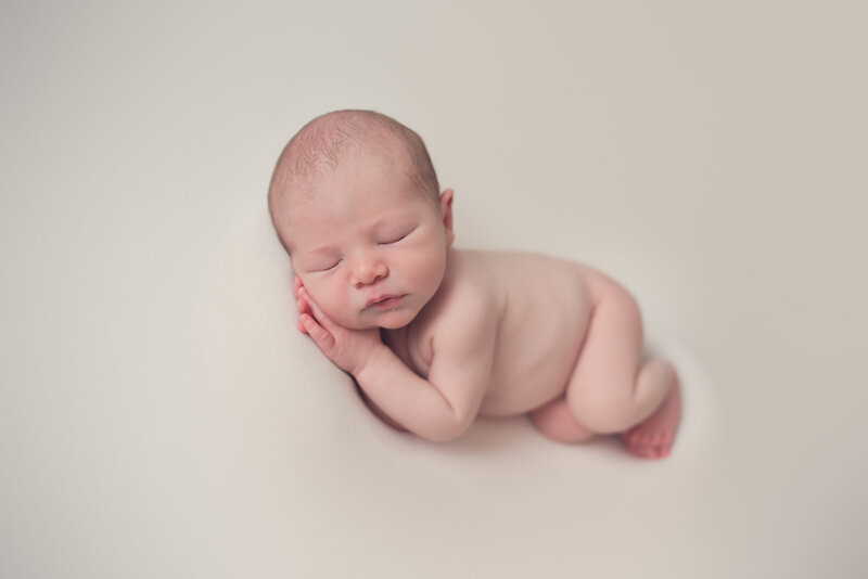 Newborn baby boy posed plain cream backdrop while sleeping and posed in side laying pose