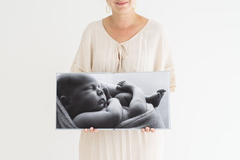 Photo of baby photographer holding newborn photo album with image of newborn baby in black and white