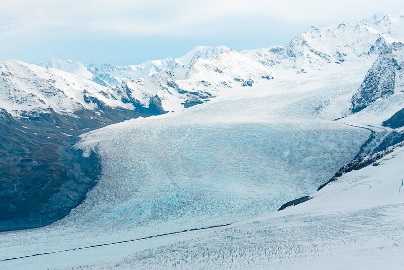 A sweeping view of the Knik Glacier ice falls taken from a helicopter on the way to an elopement vows ceremony on a the glacier during an Alaska Glacier Wedding.  with mountains, covered with snow, on the edge of the glacier valley.  