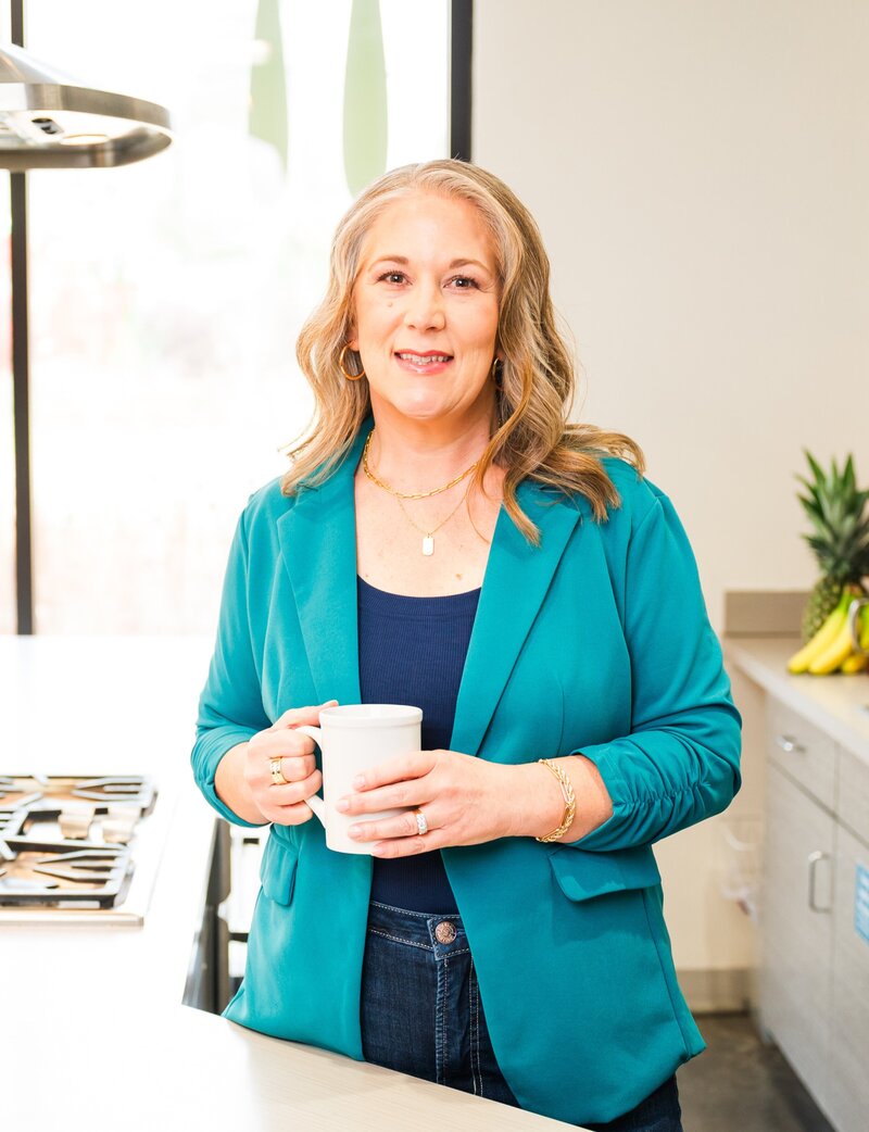 Woman in a teal blazer holding a white mug.