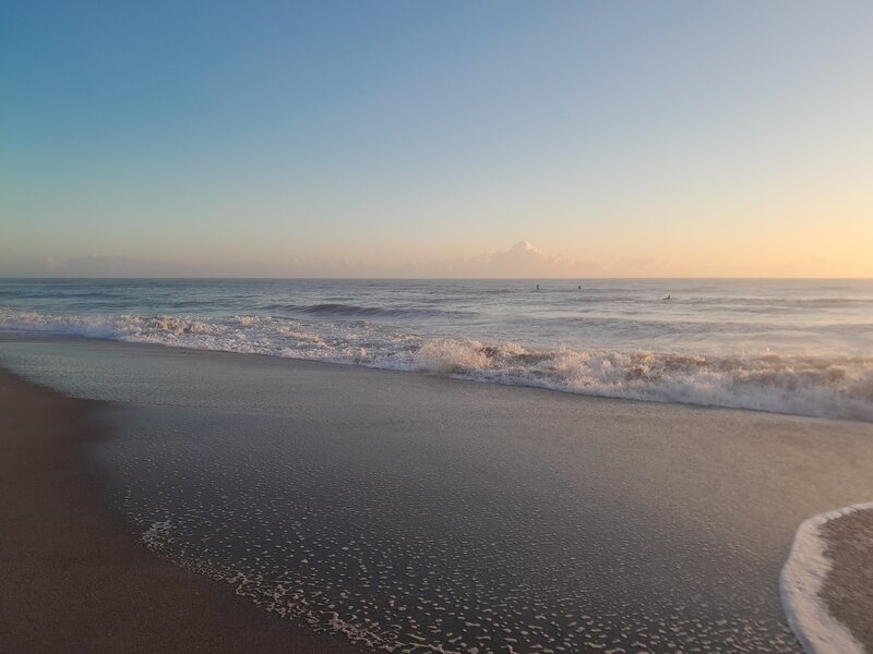 A young woman gazes off towards the sunset while she sits on an edge overlooking water/