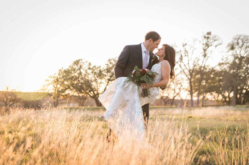 groom dips bride in field of grass