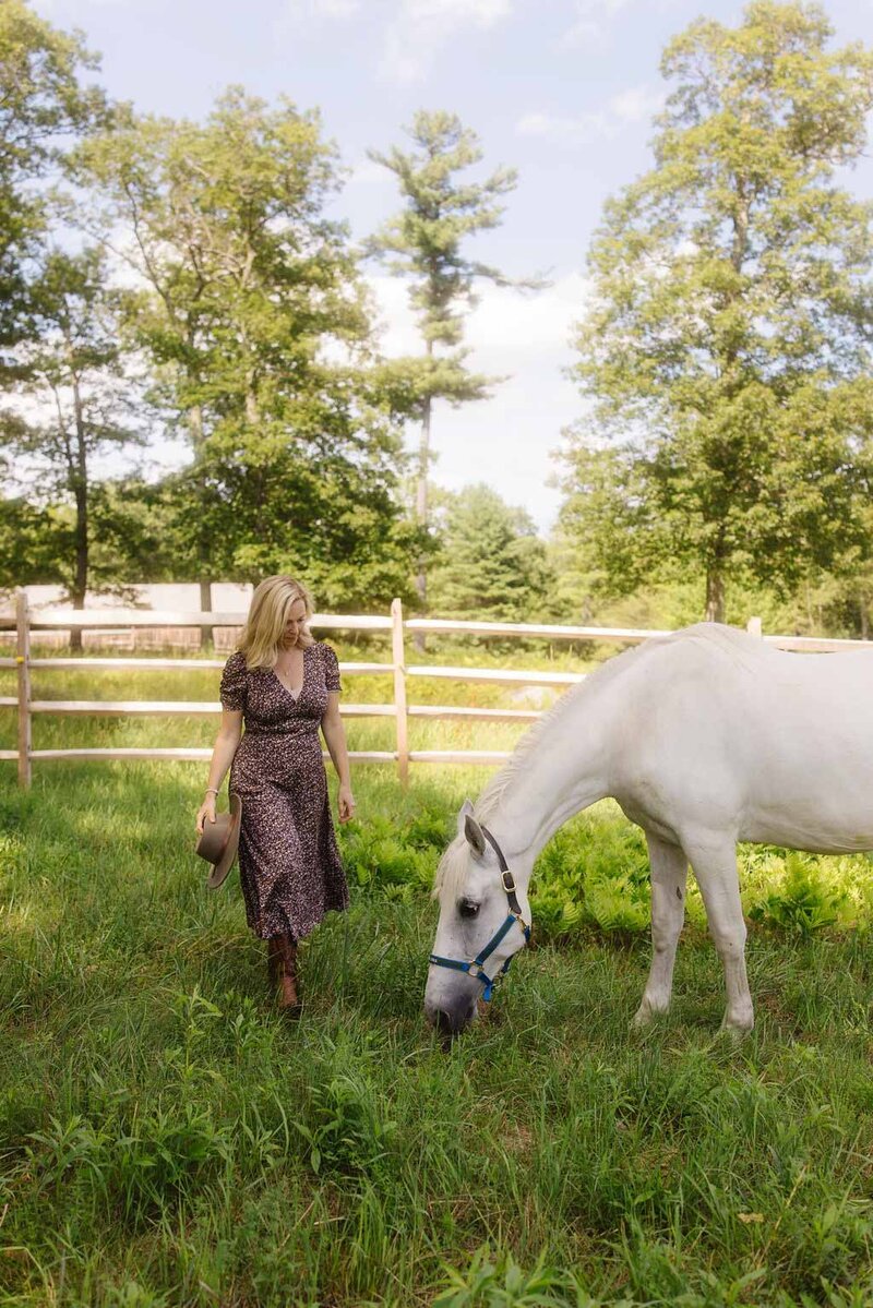 Leiko walking in a grassy field with her white horse during an equine-guided healing moment