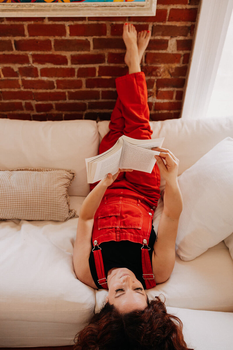 A GIF of a woman laying on a couch with her feet up reading a book.