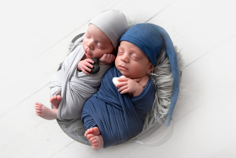 Twin newborn boys swaddled and posed in tub during photo shoot.