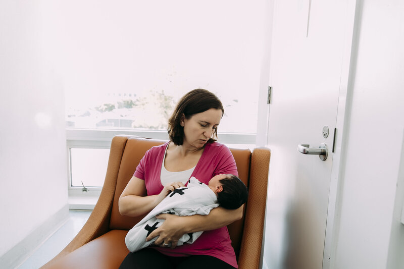 Midwife cradling a newborn wrapped in a patterned blanket during a postpartum visit