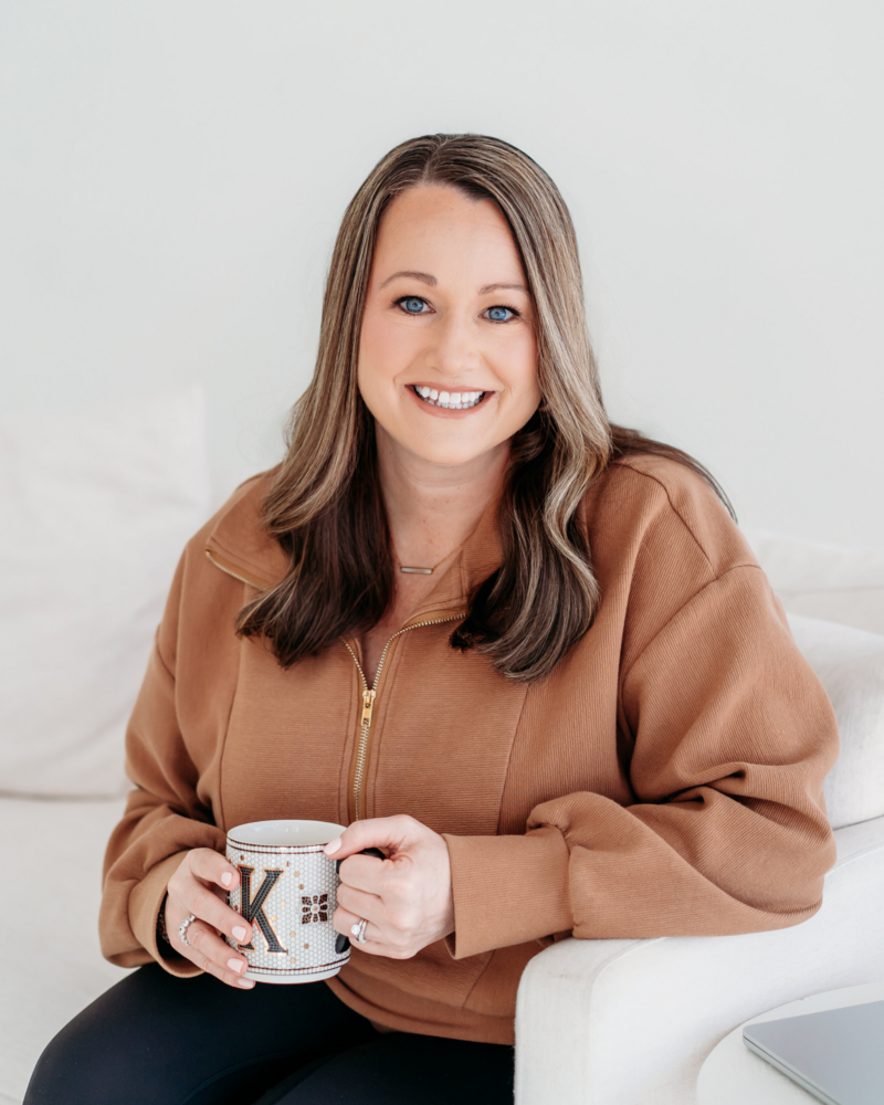 Kim sitting on the couch smiling as she holds a cup of coffee