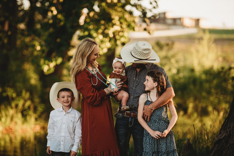 woman in dress man with white shirt and jeans two children with denim overalls standing in a grass field posing for a family photo