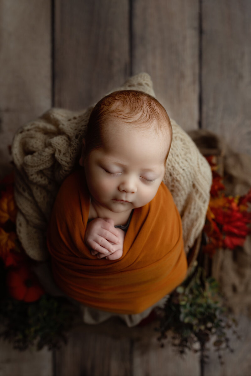 Newborn closeup in burnt orange, styled with fall textures and neutral knits for a cozy seasonal session.
