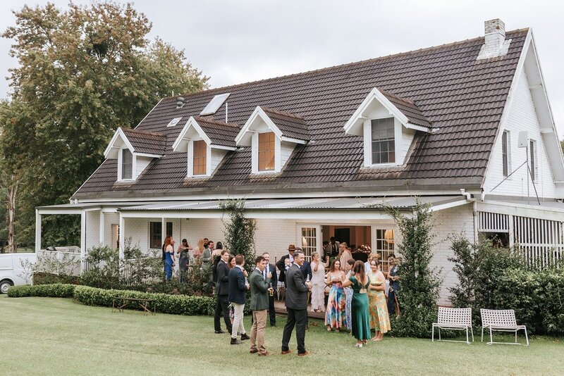 A house with a group of wedding guests mingling out the front on manicured lawns