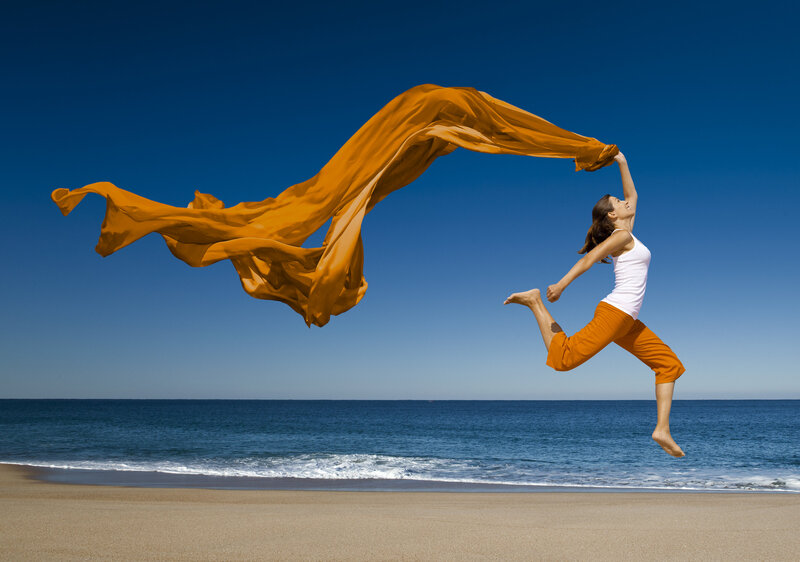 Woman in exercise clothing throws orange fabric alongside the beach.