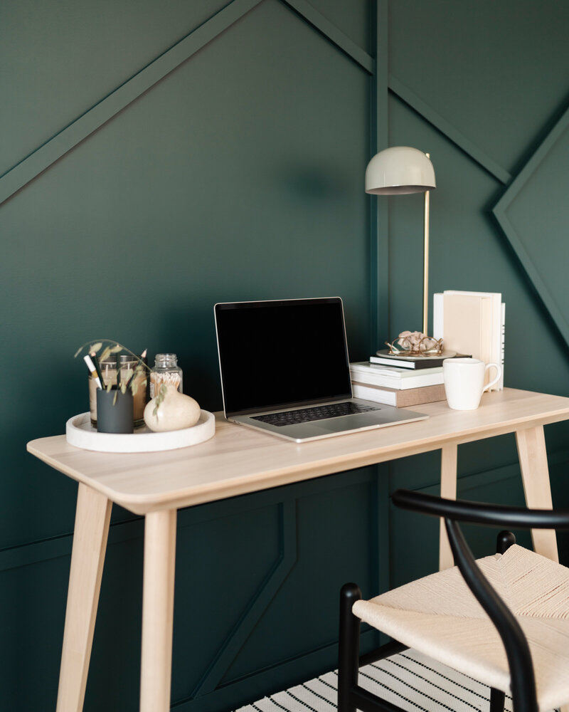 Es steht ein Schreibtisch an der Wand, davor ein Stuhl in Beige. Auf dem Schreibtisch stehen ein Laptop, eine Lampe und Deko.