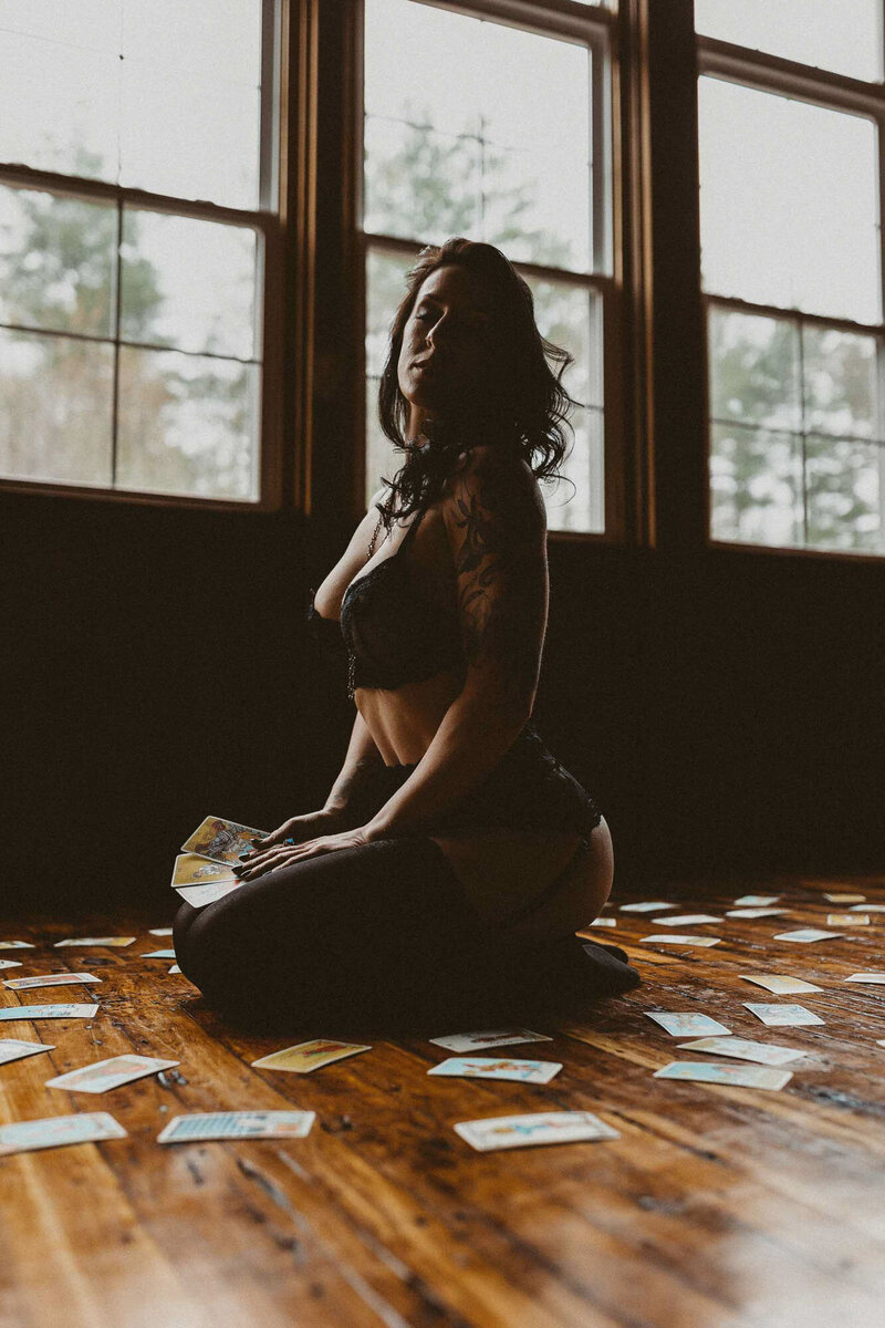 woman in a black lingerie sitting on the floor while holding a tarot cards