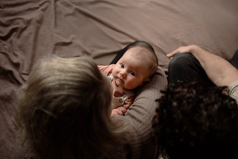 Gezicht van baby tussen de hoofden van ouders in tijdens een newbornshoot