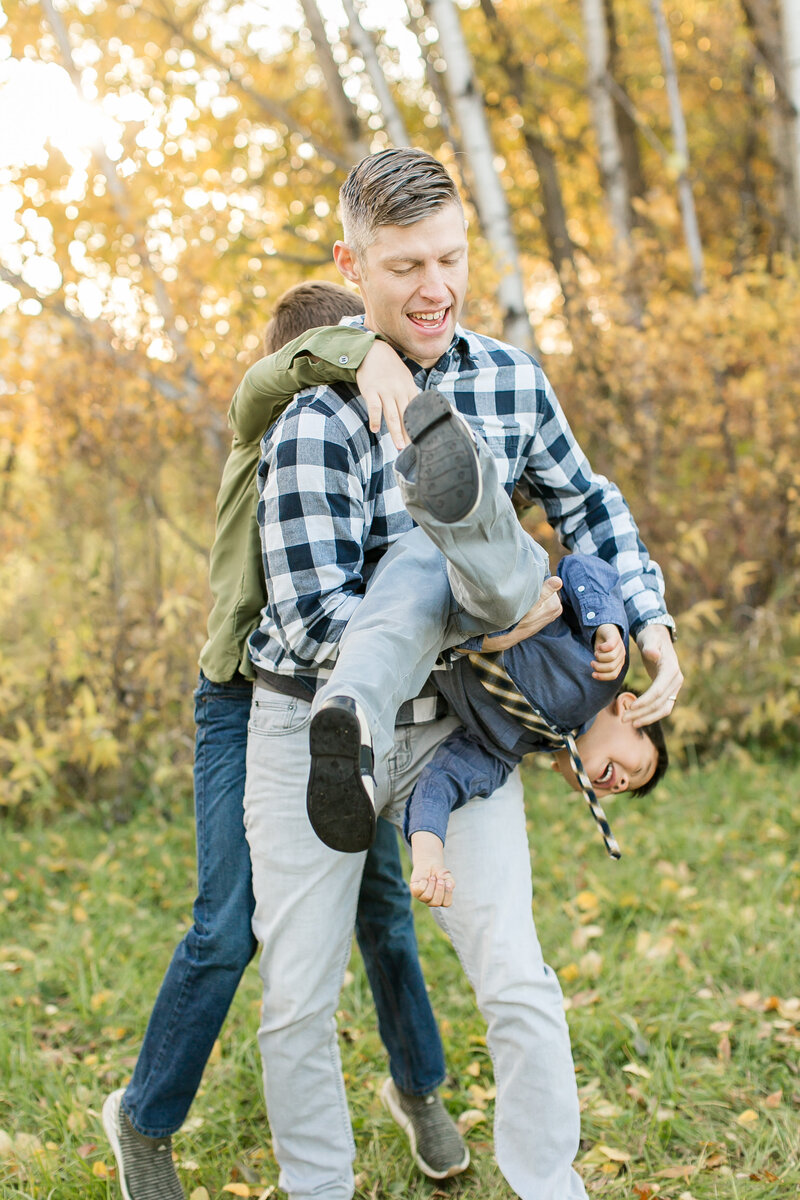 A dad and his two sons are standing and playfully wrestling