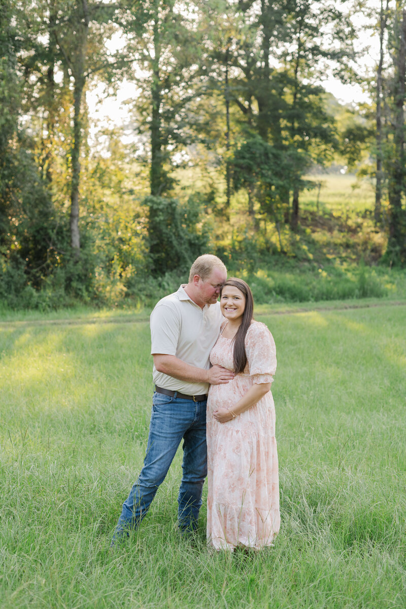 Dothan Alabama couple posing in a field for Maternity photos smiling at the camera