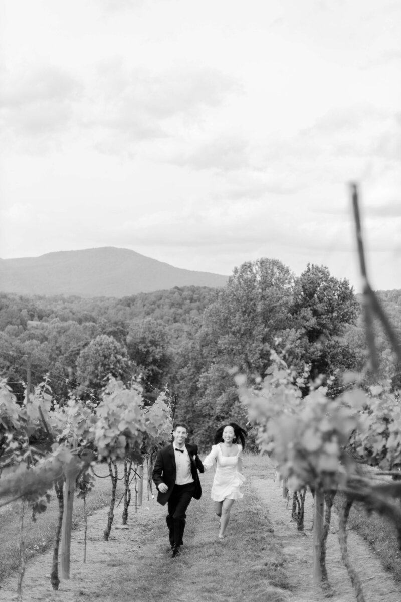 An engaged couple runs through a vineyard, backdropped by North Georgia mountains.