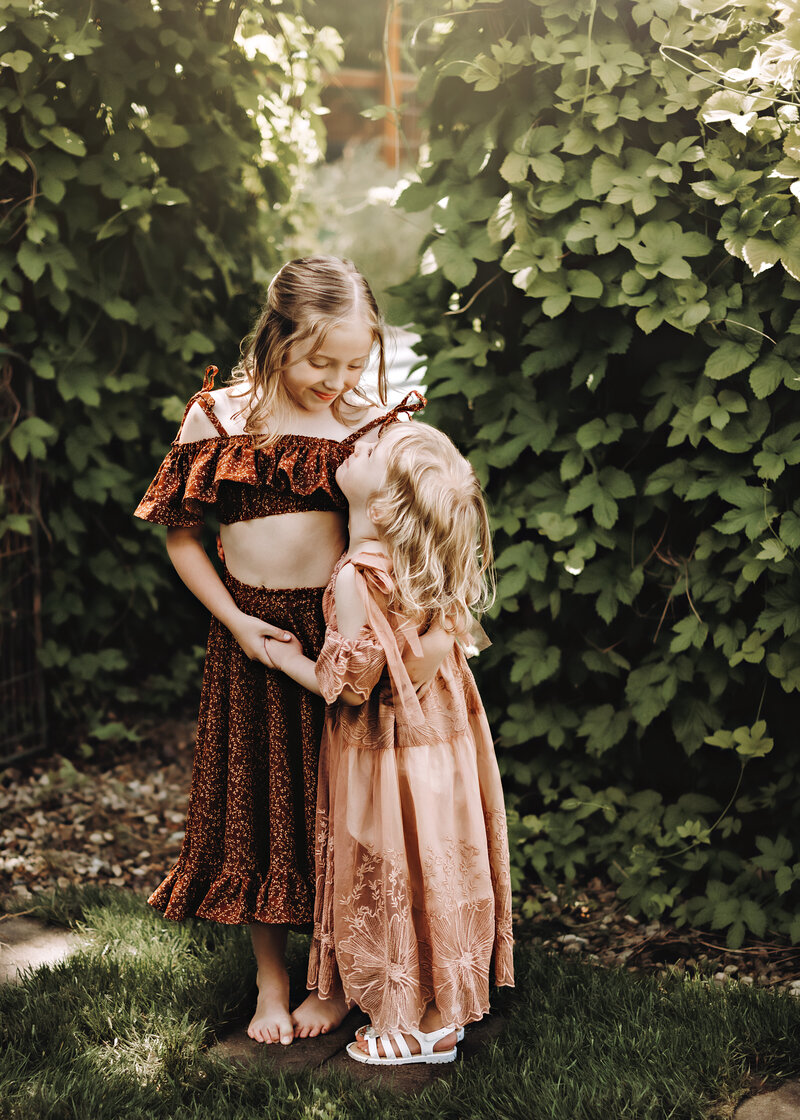 Two sisters look at each other and hold hands in front of an ivy tunnel at the Urban Farmhouse in Boise Idaho