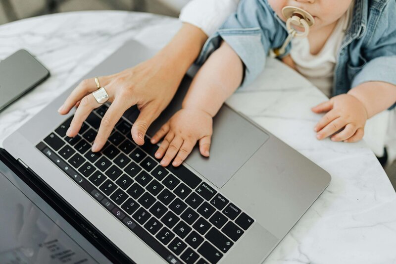 Image of the hand of a mom and the hand of a small child on her lap reaching for a laptop keyboard