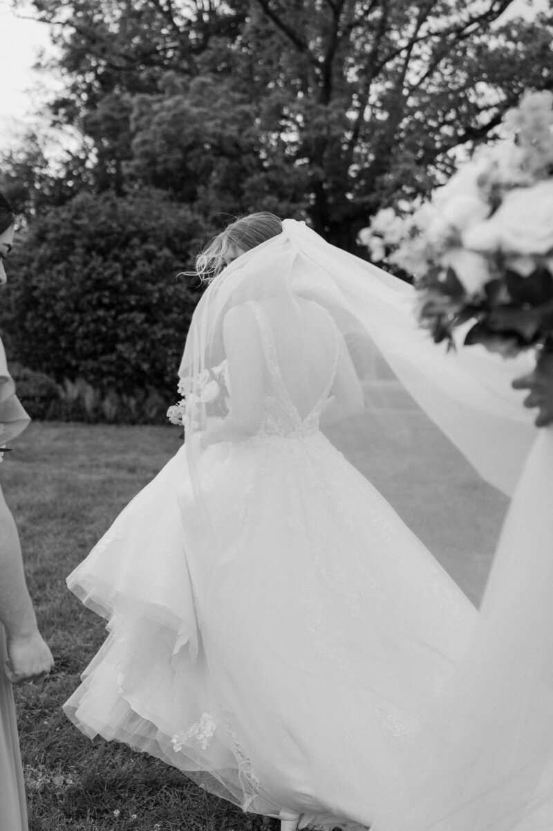 Close-up photograph of bride (long sleeve sheer wedding dress) standing by a window