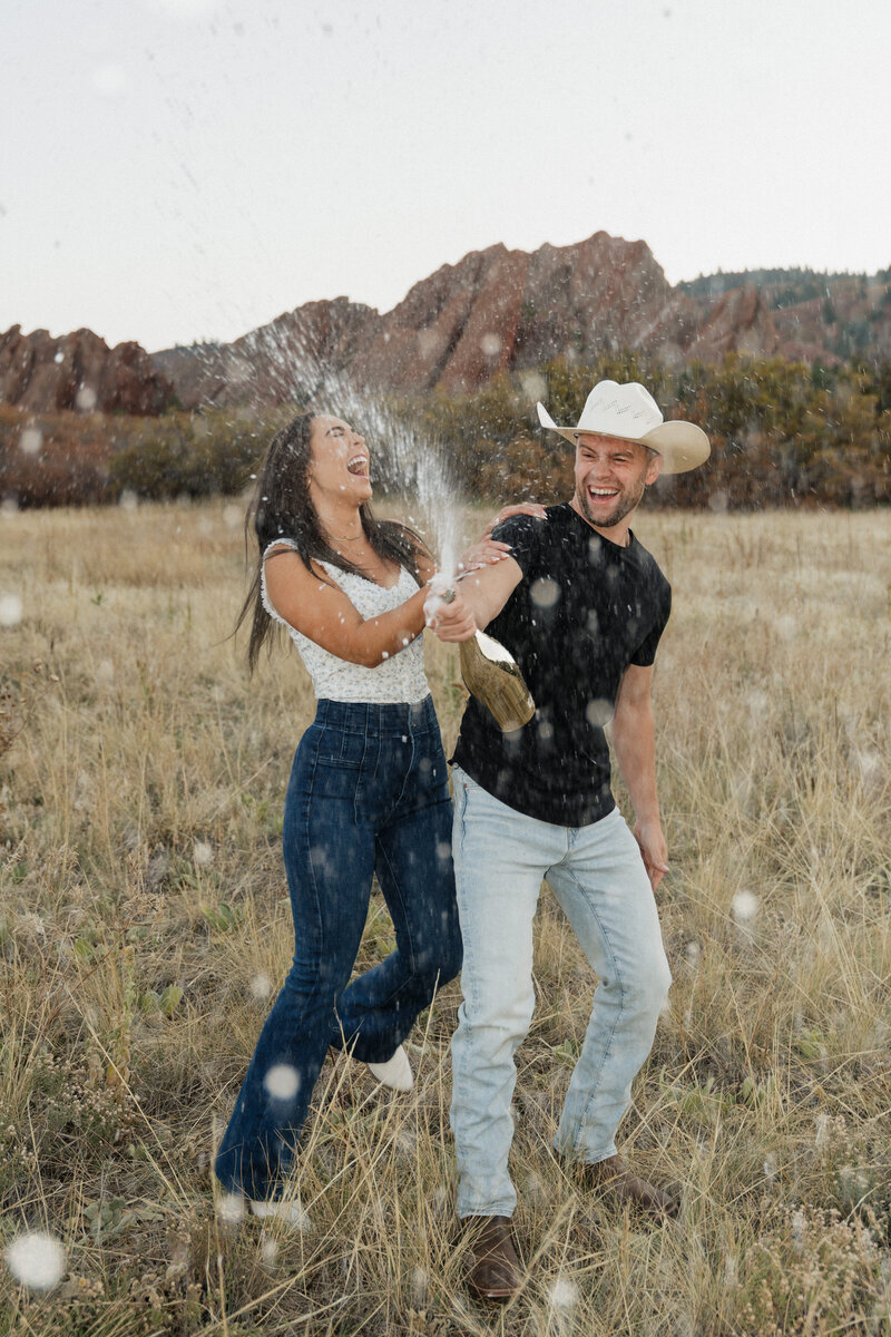man and woman popping a bottle of champagne while laughing