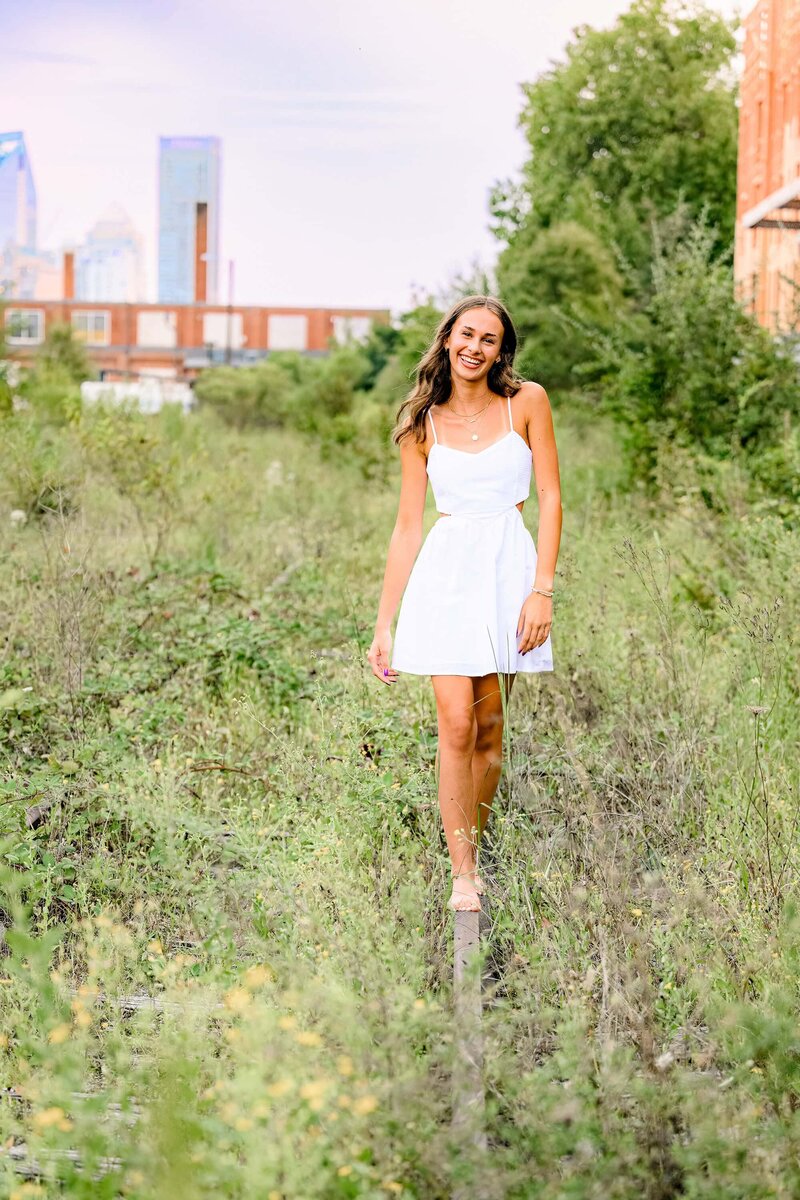 walking senior images of grad in white dress with long dark hair