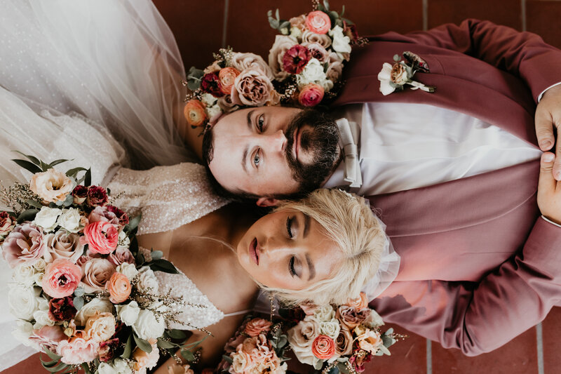 Bride and groom laying head to head, surrounded by flowers