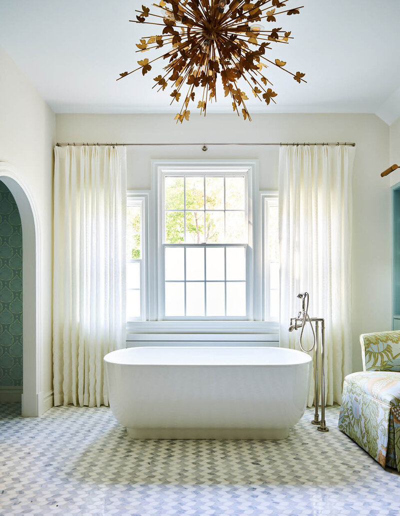 Boston kitchen and bath designer created a custom primary bathroom with a gilded light fixture, freestanding tub, and linen embroidered drapery panels.